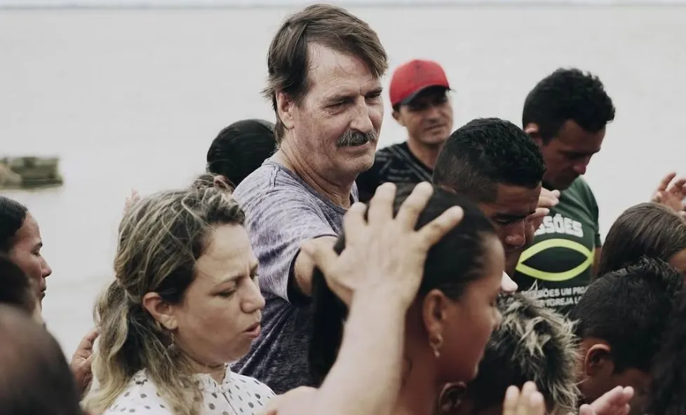 Missionário orando com um grupo de pessoas às margens do rio